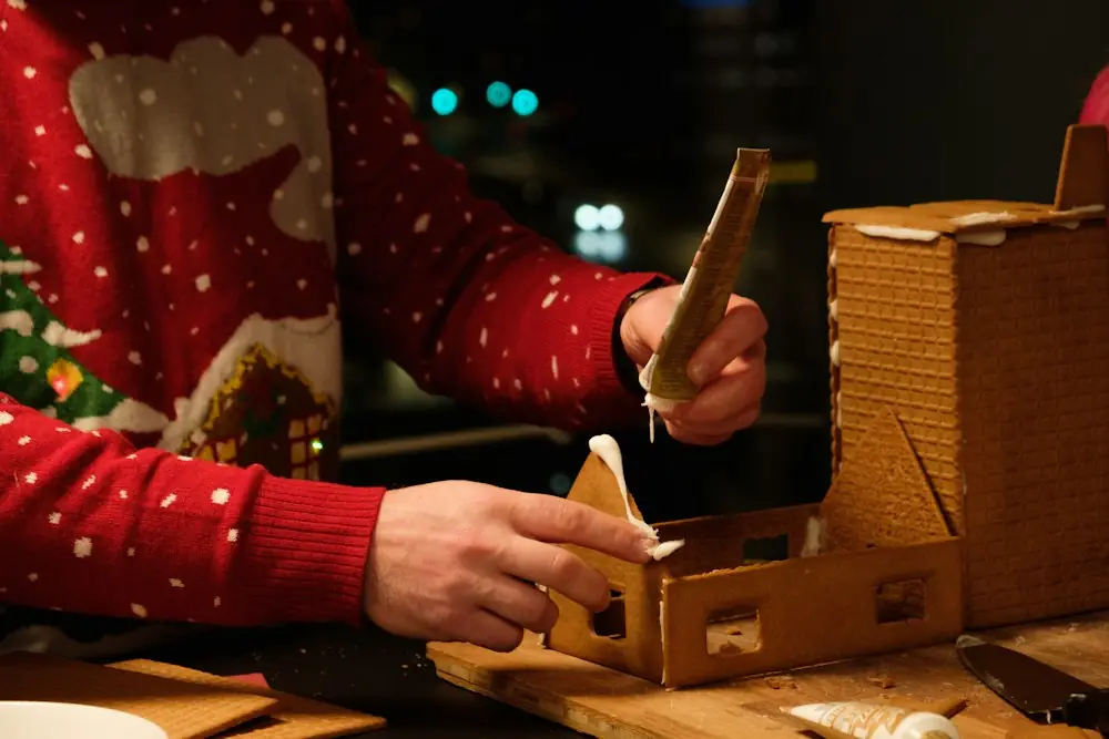 Arms in a red reindeer-pattern sweater building a gingerbread house