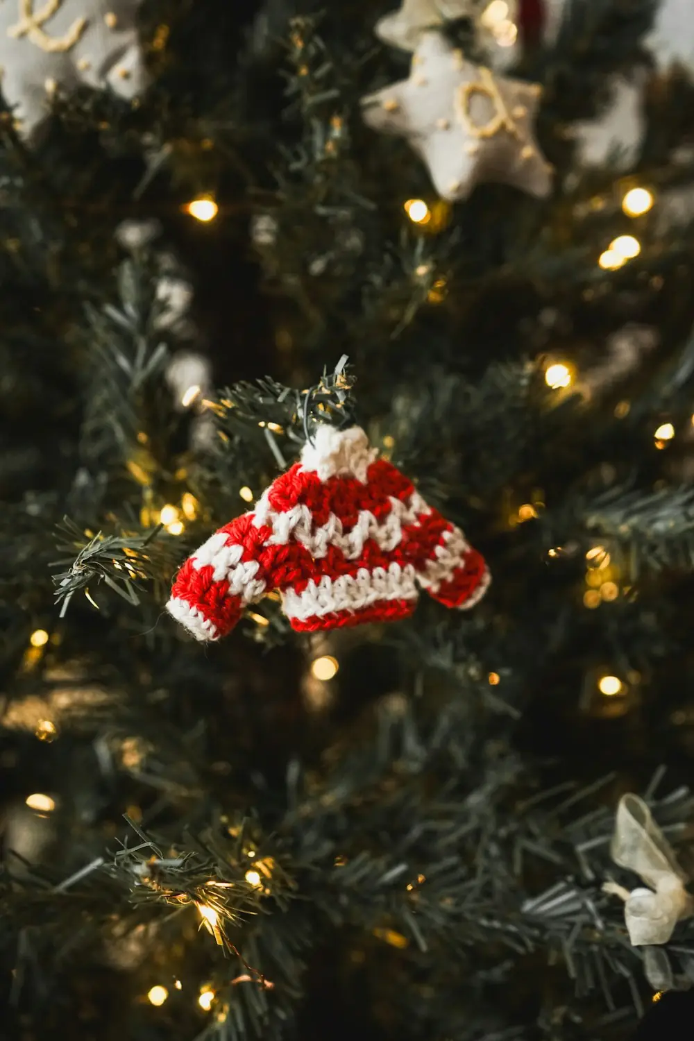 A tiny red and white knitted sweater ornament hanging on a lit Christmas tree